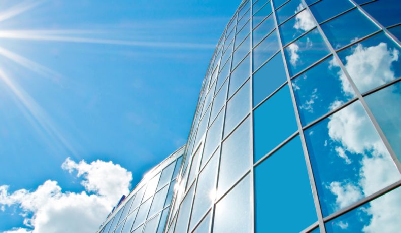 moderne glasfassade mit sonnenspiegelung bei strahlendem sonnenschein – symbol für effektiven hitze- und uv-schutz durch hochwertige sonnenschutzfolien