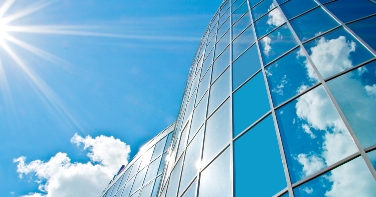 moderne glasfassade mit sonnenspiegelung bei strahlendem sonnenschein – symbol für effektiven hitze- und uv-schutz durch hochwertige sonnenschutzfolien